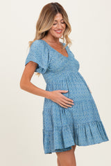 woman wearing a blue floral maternity dress with puff sleeves, smiling and holding her baby bump