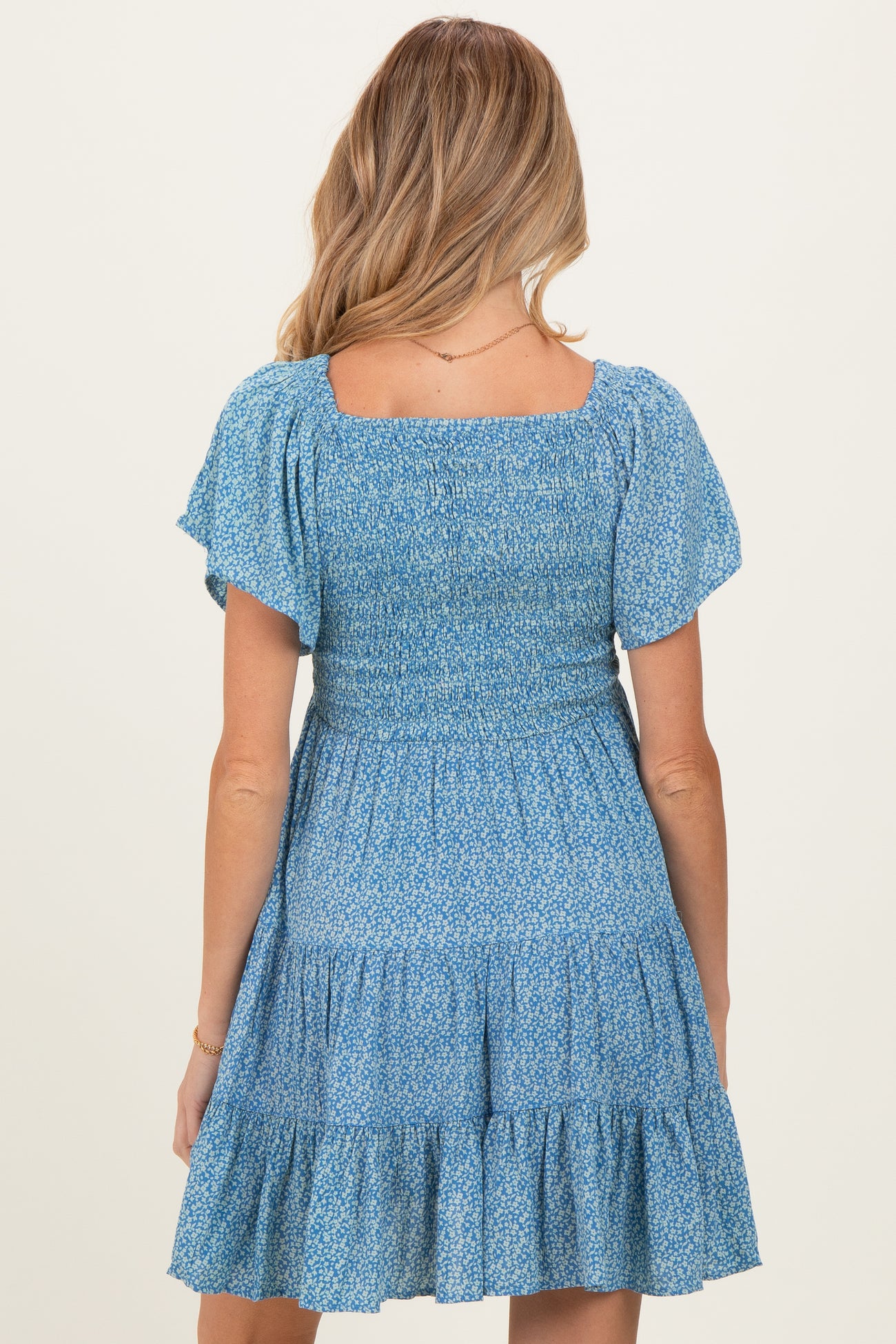 woman wearing a blue floral smocked maternity dress with short sleeves and a tiered skirt from the back