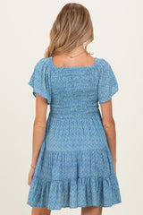 woman wearing a blue floral smocked maternity dress with short sleeves and a tiered skirt from the back