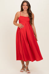 woman wearing a red maternity dress with adjustable straps, showing a visible baby bump and a flowy skirt