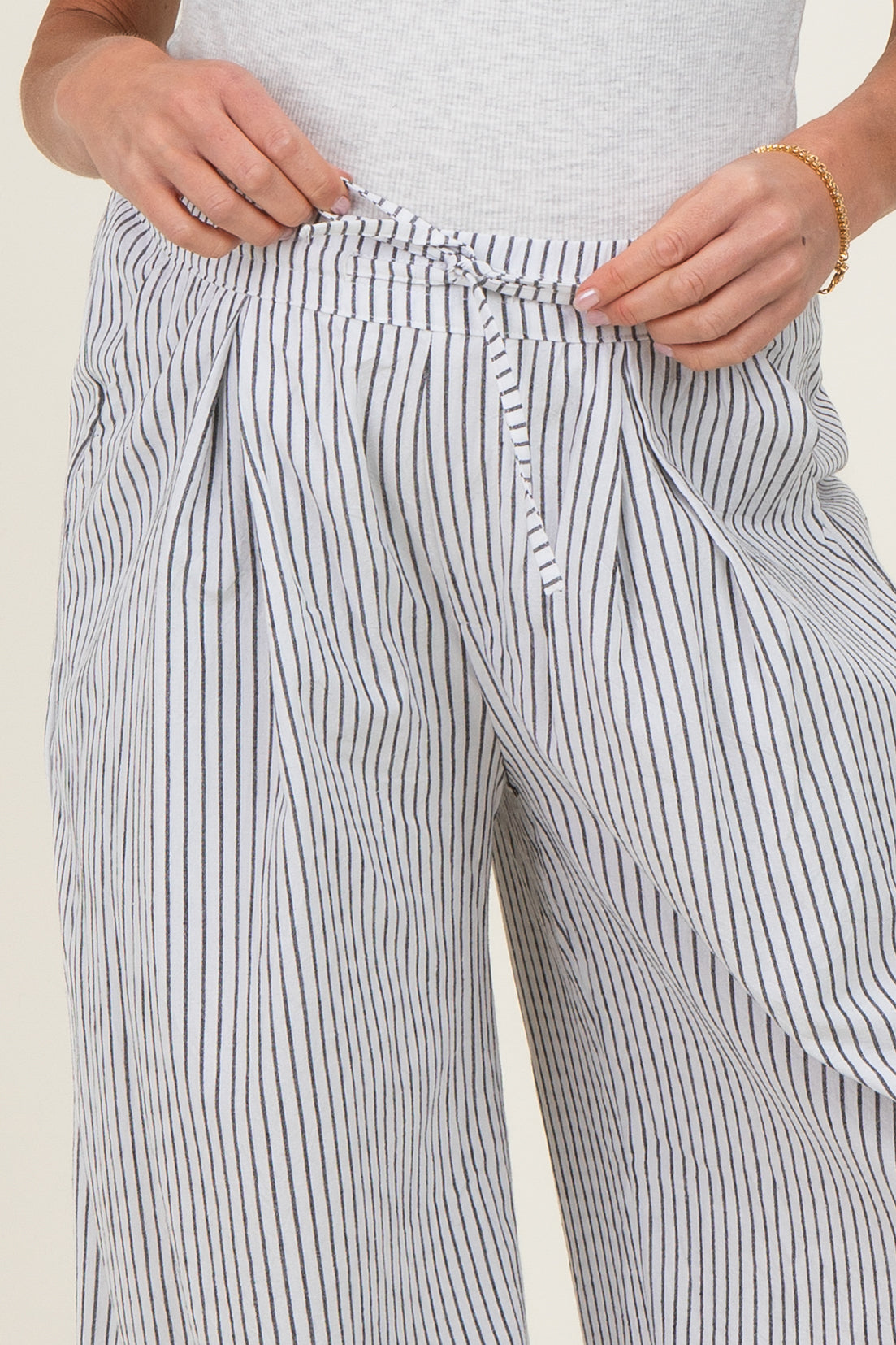 woman wearing striped maternity pants with a drawstring waist, hands holding the waistband