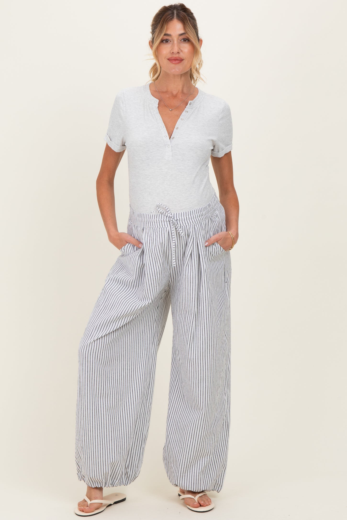 woman wearing a gray short sleeve maternity top and striped wide-leg maternity pants with pockets