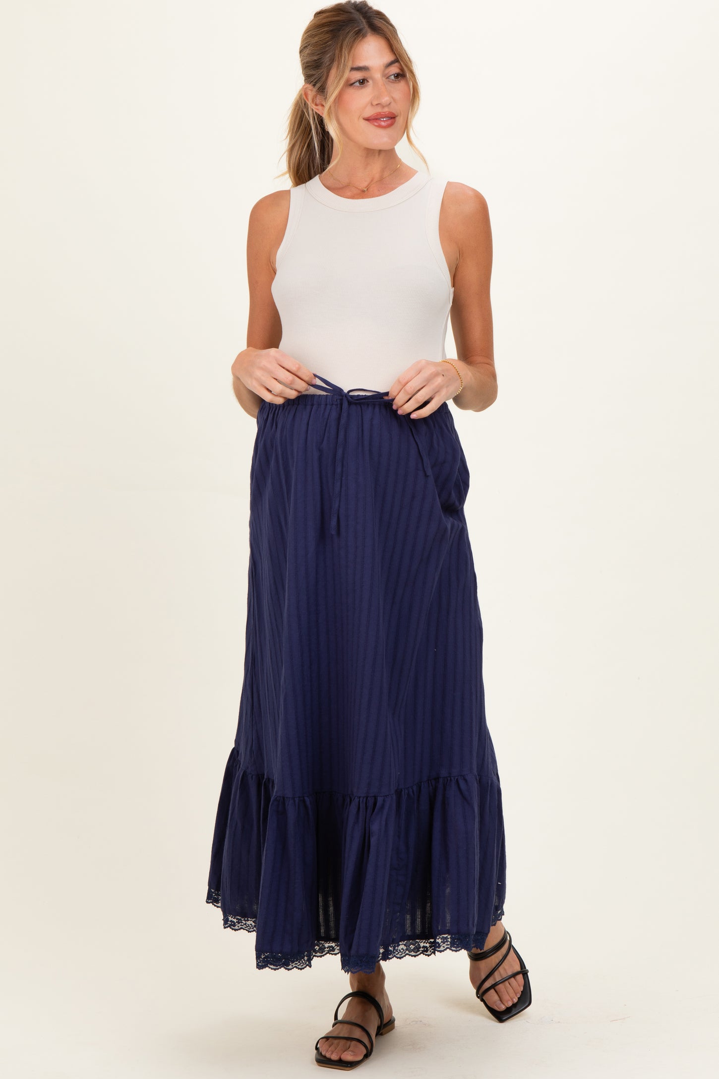 woman wearing a white sleeveless top and a navy blue striped maternity maxi skirt with a tie waist and lace hem
