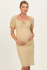 woman wearing a beige polka dot maternity dress with puff sleeves and a fitted silhouette, holding her baby bump