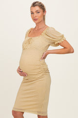 woman wearing a yellow polka dot maternity dress with ruched sides and puff sleeves, gently cradling her baby bump