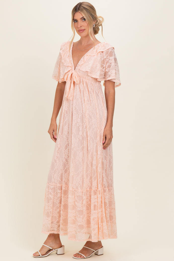 woman wearing a light pink lace maxi dress with flutter sleeves and a tie front detail