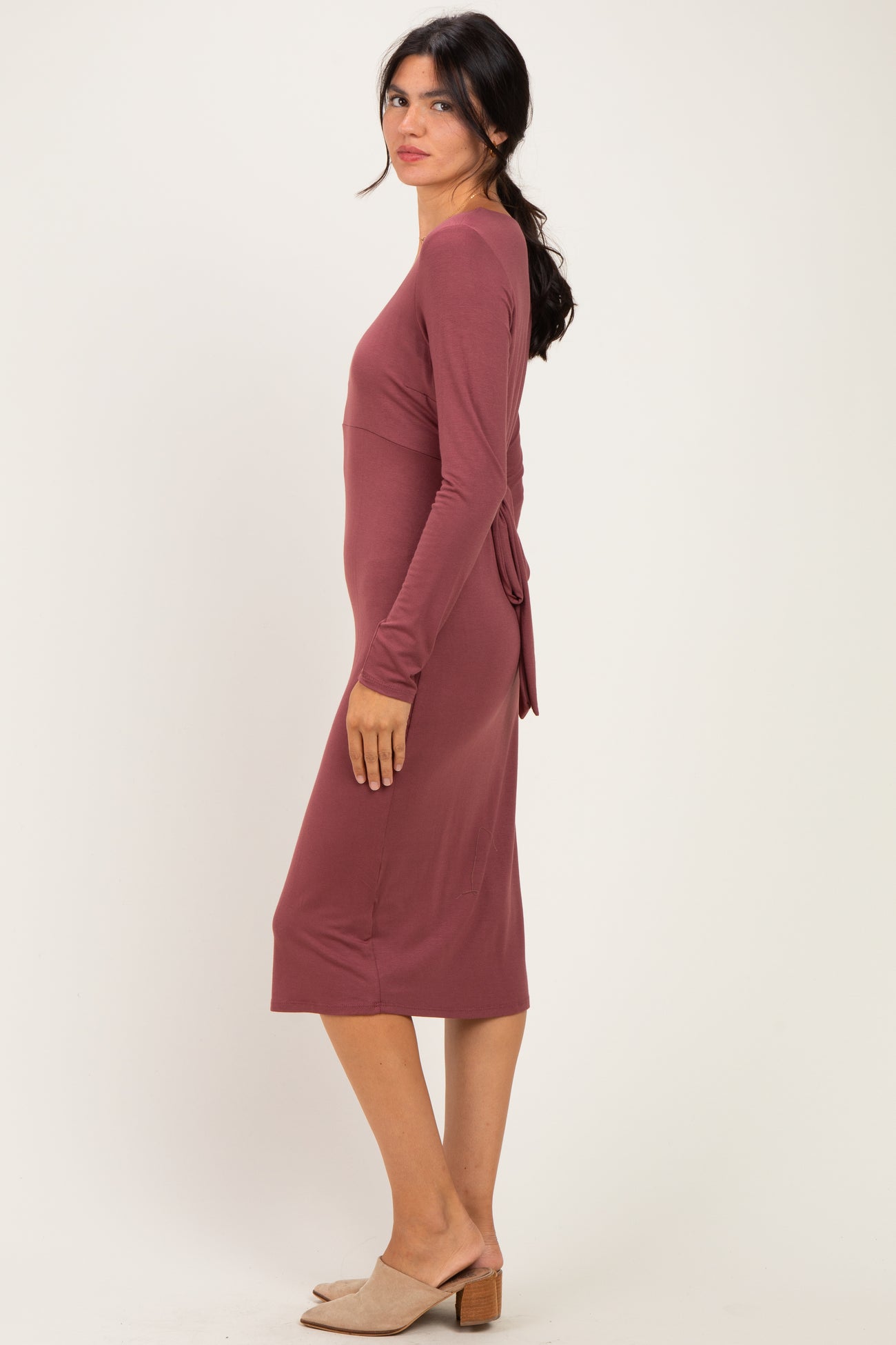 woman wearing a mauve long sleeve midi dress with a tie detail at the waist and slip-on heels