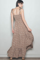 woman wearing a brown floral maxi dress with tie straps and a tiered skirt, posing with her back to the camera