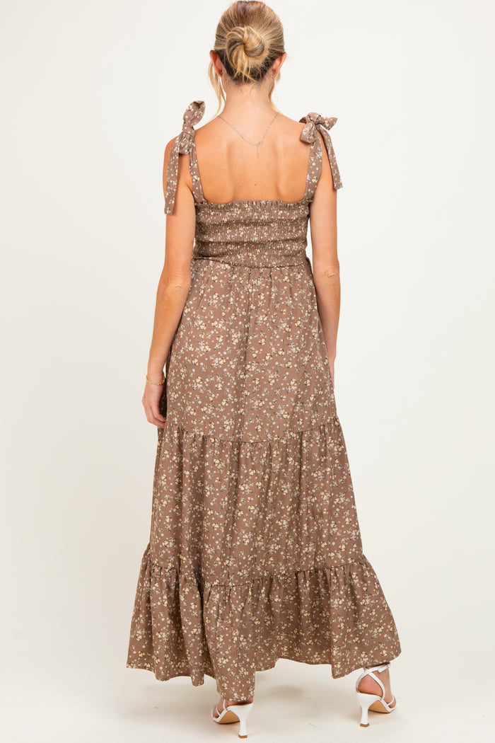 woman wearing a brown floral maternity maxi dress with tie shoulder straps, styled with a ruffled hem