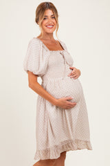 woman wearing a light beige maternity dress with smocked bodice and puff sleeves, gently cradling her baby bump