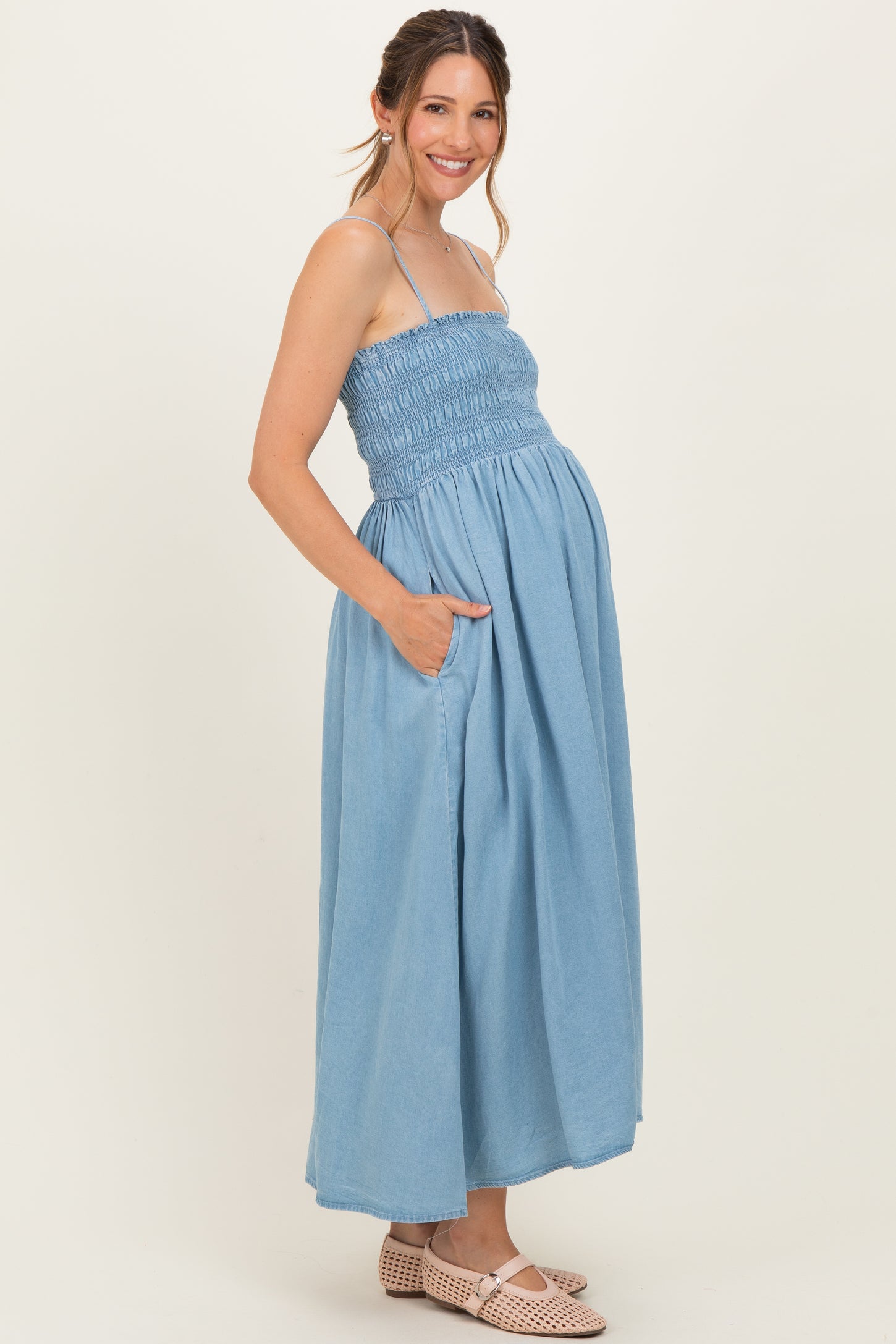 woman wearing a light blue smocked maternity maxi dress with pockets and a visible baby bump