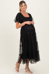 woman wearing a black maternity maxi dress with a square neckline and tiered tulle detailing, showcasing her baby bump