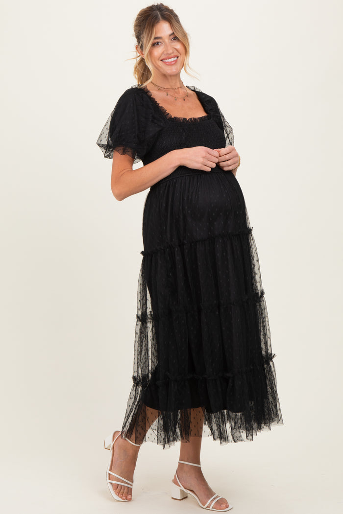 woman wearing a black maternity maxi dress with a square neckline and tiered tulle detailing, showcasing her baby bump