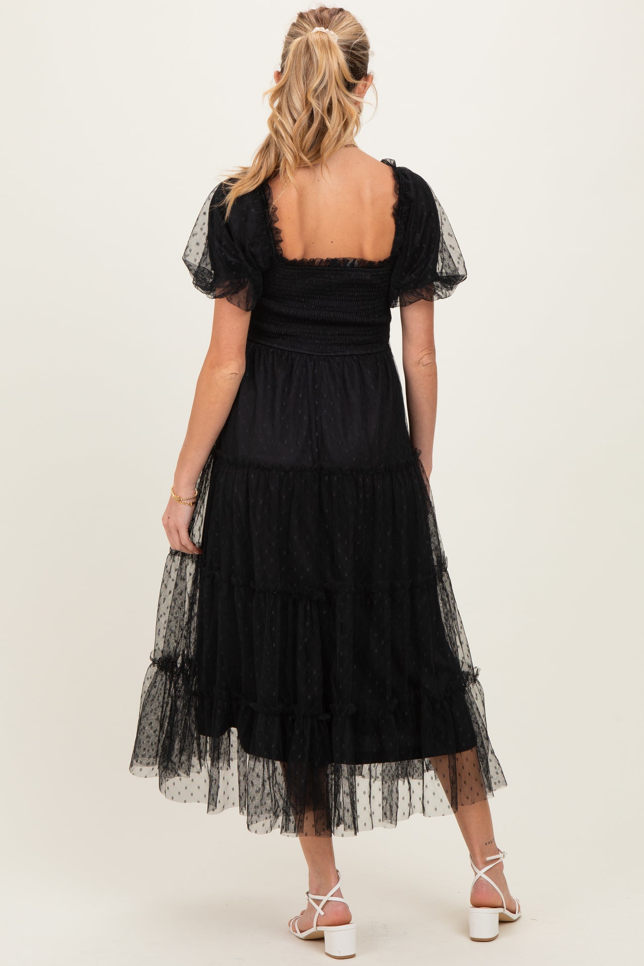 woman wearing a black maternity dress with short puff sleeves and a tiered skirt, showing her baby bump from the back