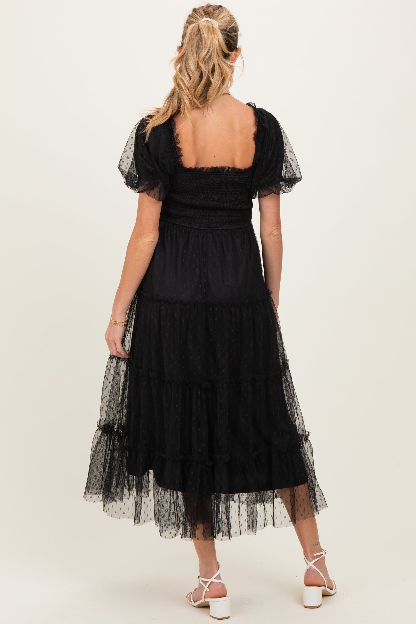 woman wearing a black maternity dress with short puff sleeves and a tiered skirt, showing her baby bump from the back
