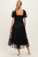 woman wearing a black maternity dress with short puff sleeves and a tiered skirt, showing her baby bump from the back