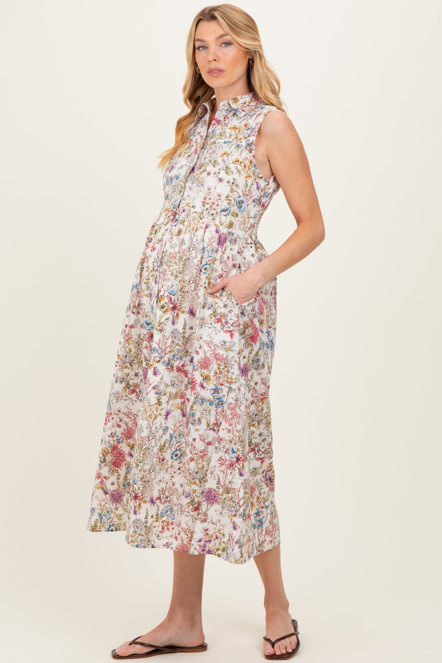woman wearing a floral print sleeveless maternity dress with a button-down front and side pockets