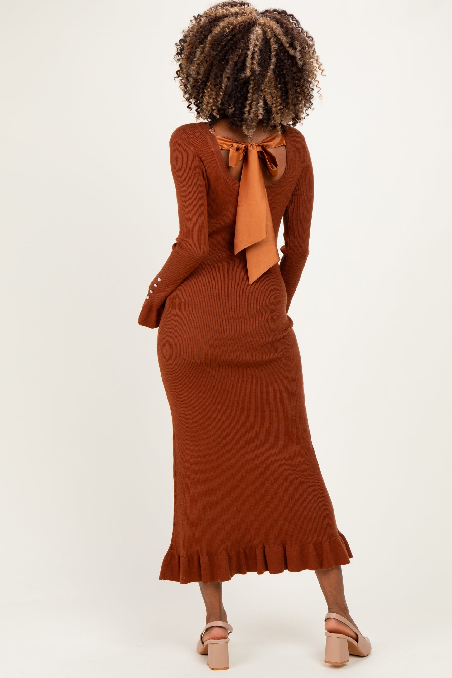 woman wearing a rust ribbed maternity dress with a tie detail at the back and ruffled hem