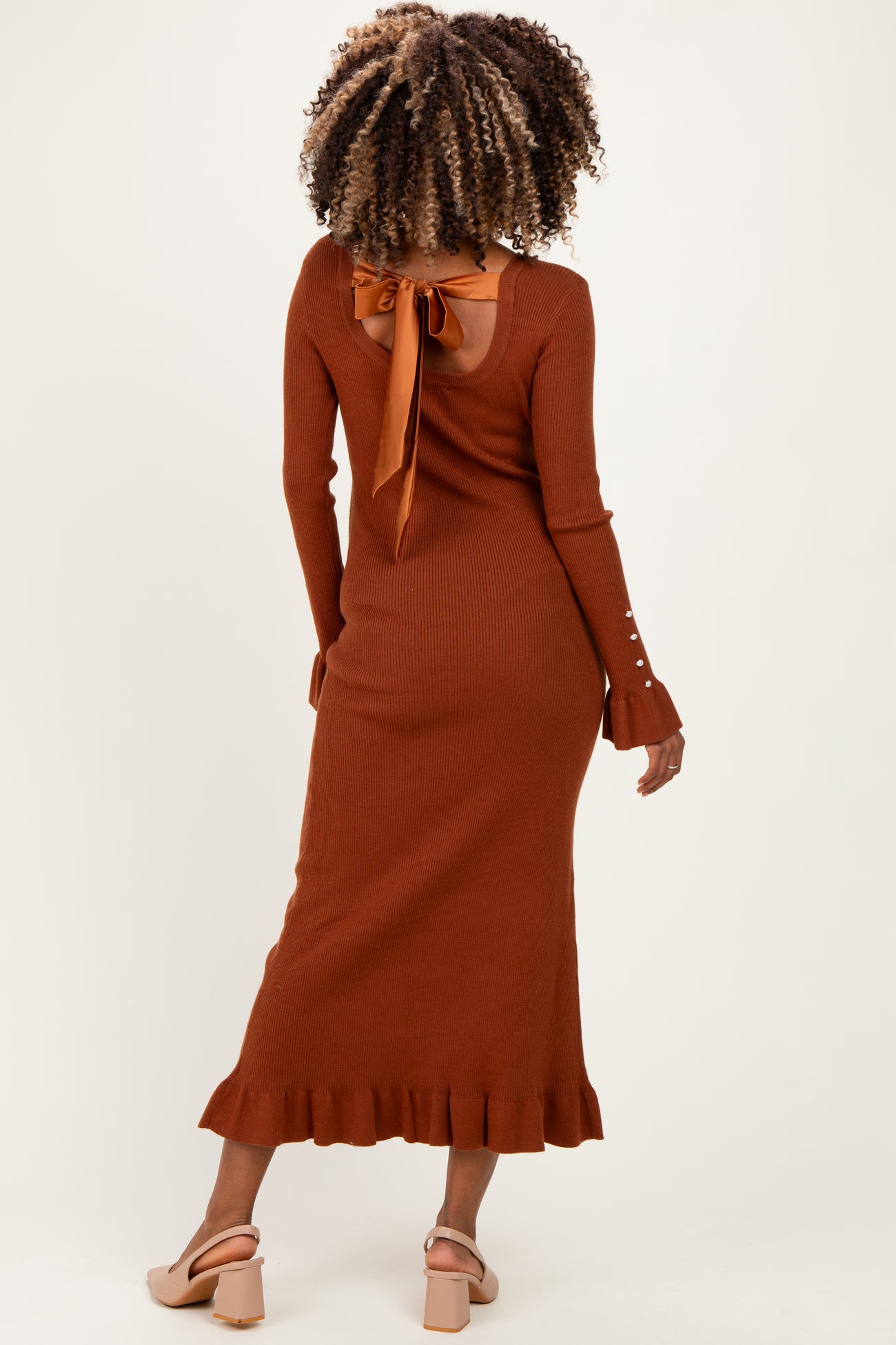 woman wearing a rust-colored maternity ribbed dress with a back tie detail and ruffle hem