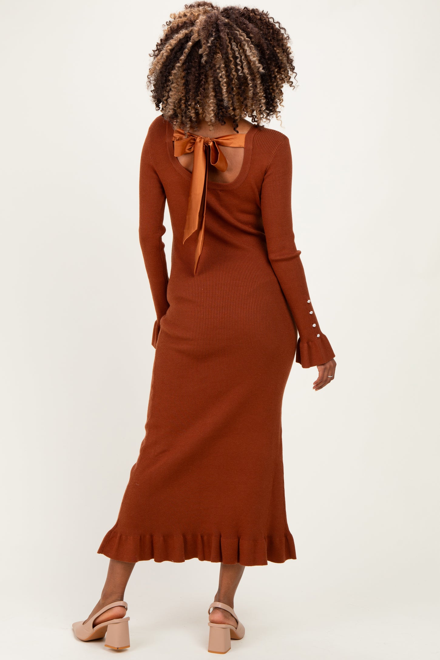 woman wearing a rust-colored maternity ribbed dress with a back tie detail and ruffle hem