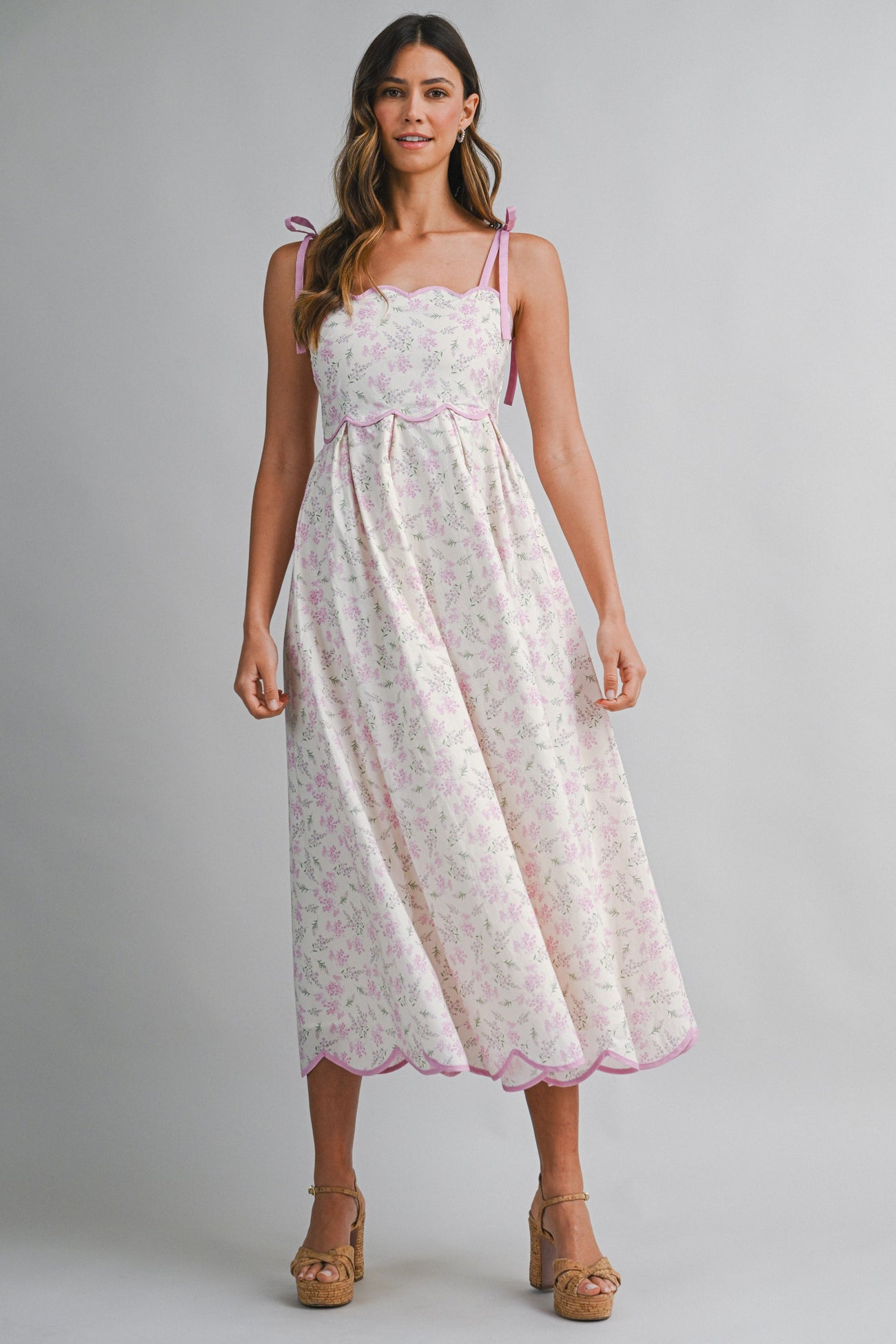woman wearing a floral print midi dress with pink scalloped edges and tie straps