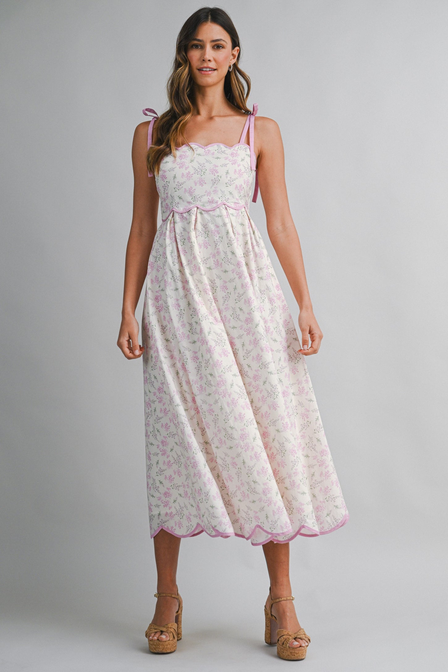 woman wearing a floral print midi dress with pink scalloped edges and tie straps