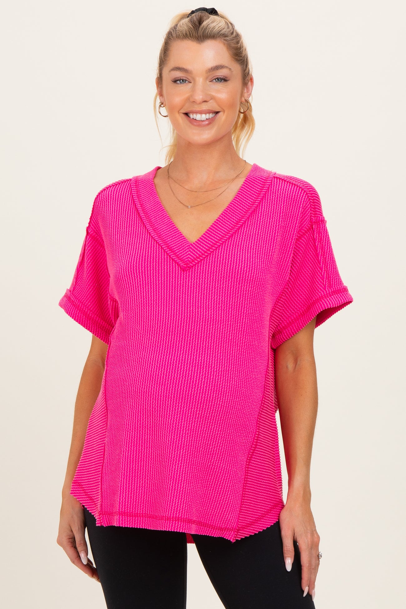 woman wearing a bright pink v-neck maternity top with rolled short sleeves and a relaxed fit