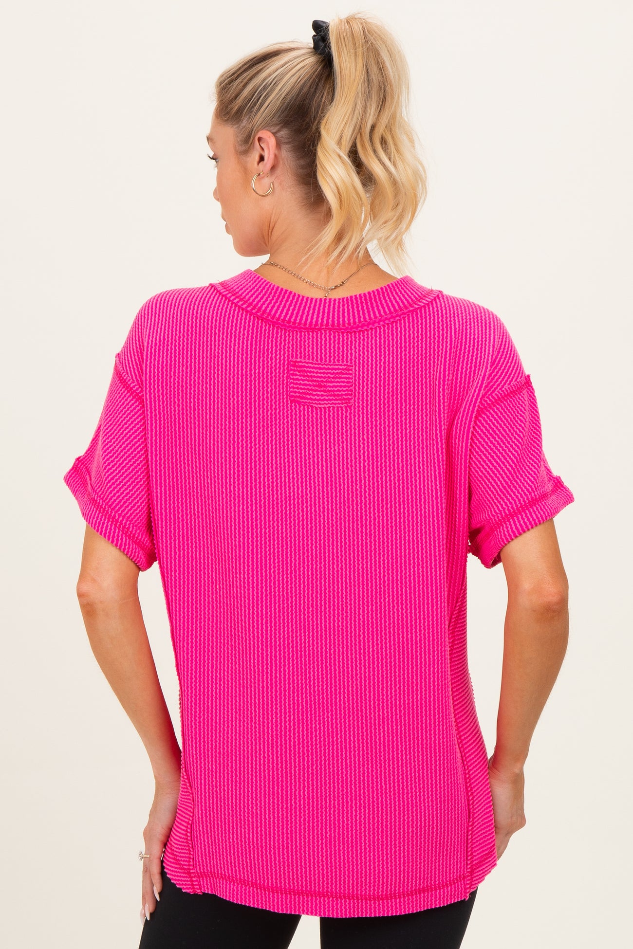 woman wearing a bright pink ribbed maternity top with rolled sleeves and a relaxed fit, showing her baby bump