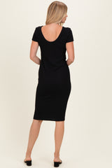 woman wearing a black ribbed midi dress with a scoop back and short sleeves, standing with her back to the camera