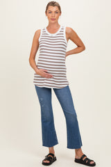woman wearing a gray and white striped maternity tank top and distressed blue flared jeans, gently holding her baby bump