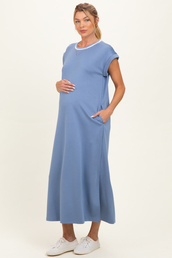 woman wearing a light blue maternity dress with short sleeves and pockets, gently cradling her baby bump