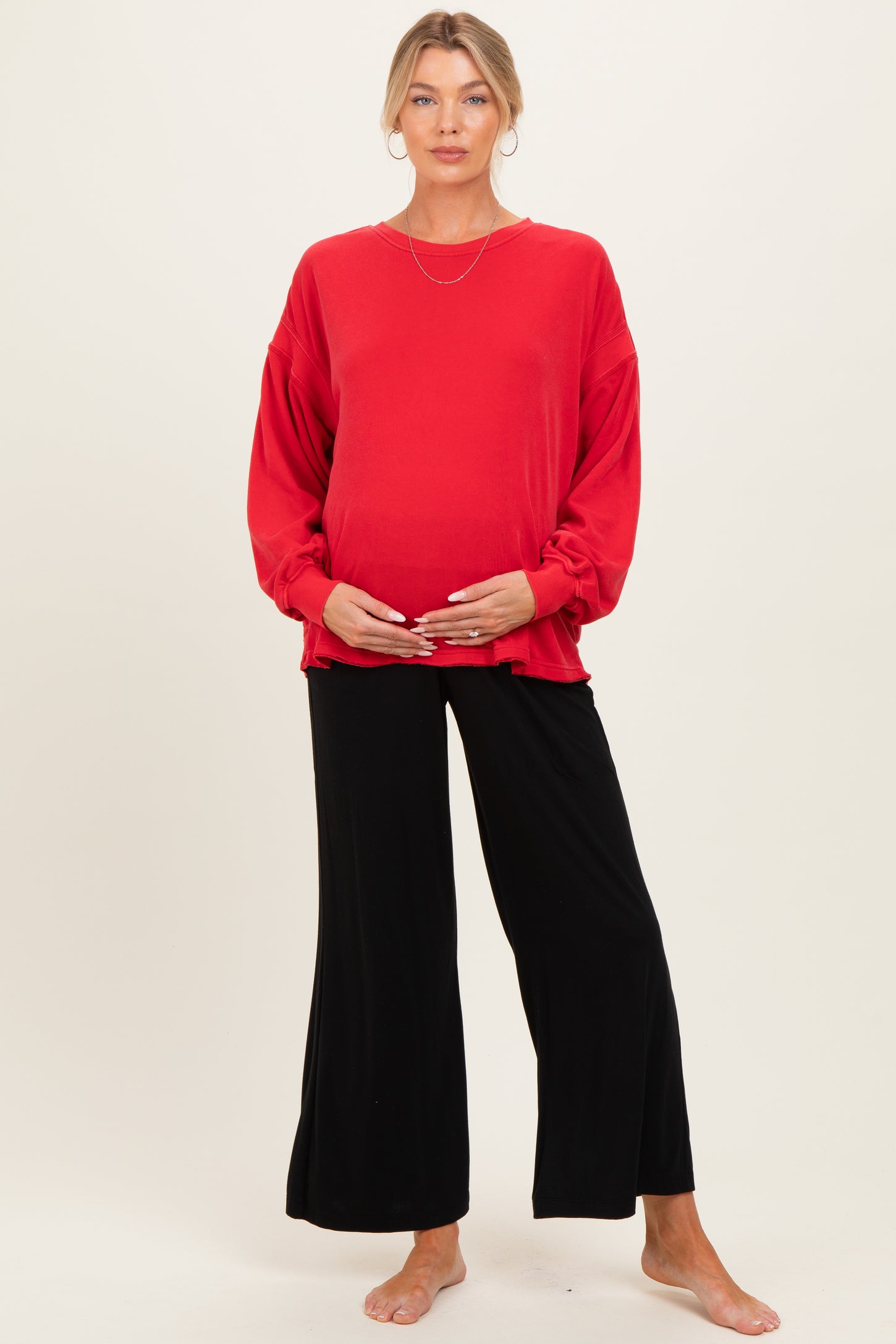 woman wearing a red oversized maternity sweater and black wide-leg pants, showcasing her baby bump