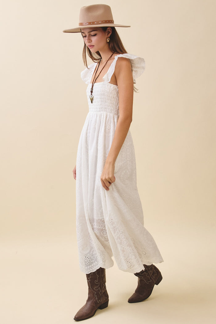 woman wearing a white maxi dress with ruffle straps and a smocked bodice, paired with a beige hat and brown cowboy boots