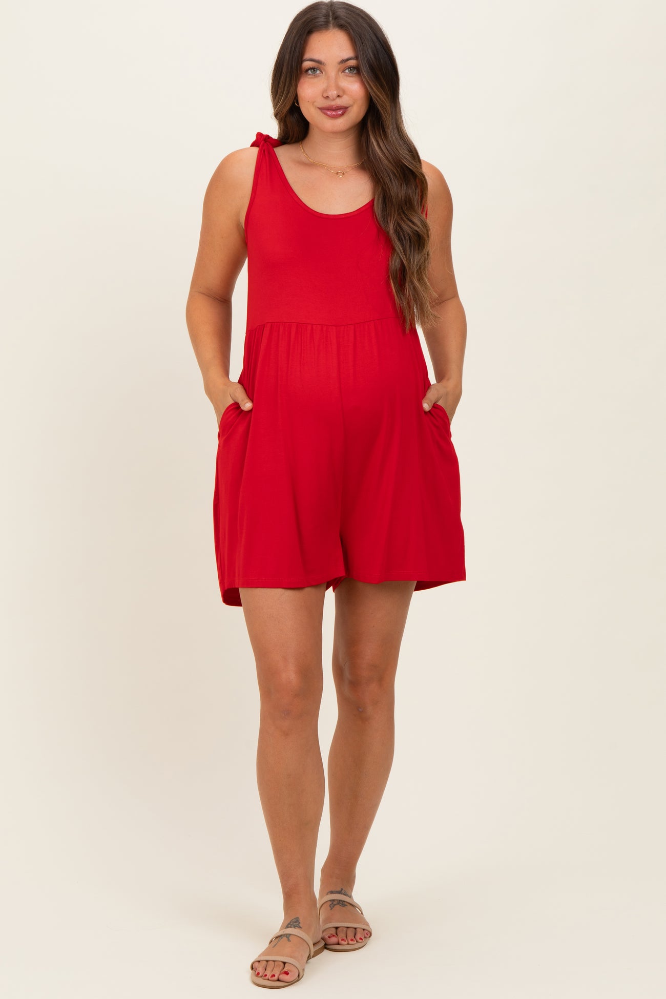 woman wearing a red maternity romper with tie straps and side pockets, showcasing her baby bump