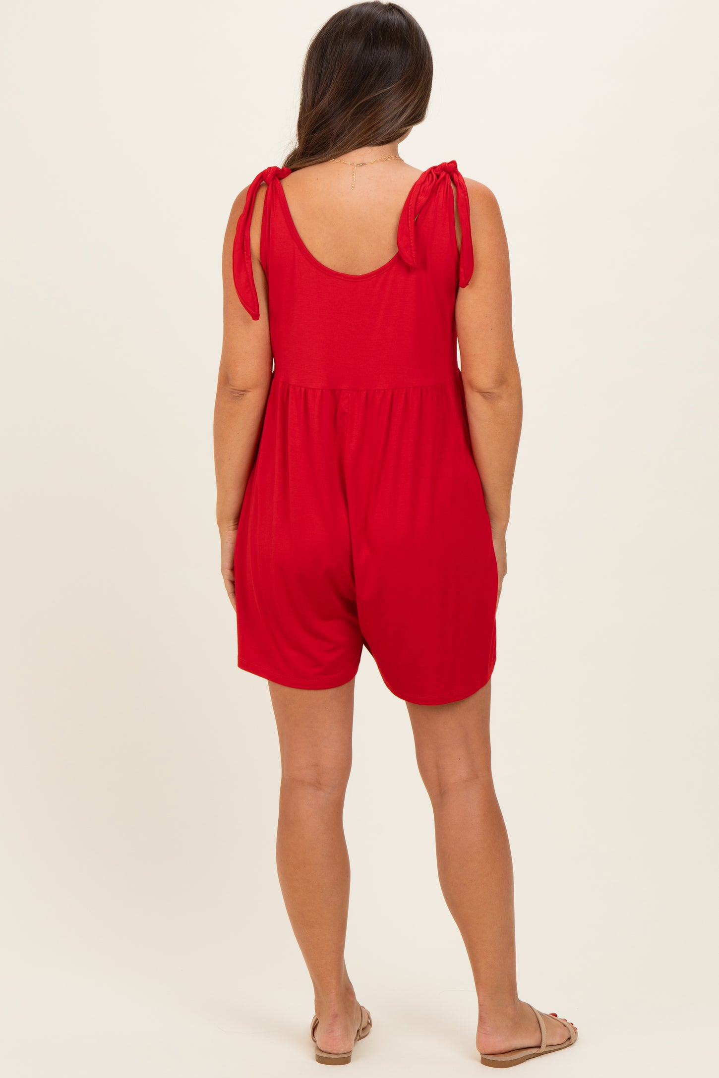 woman wearing a red maternity romper with tie shoulder details and a comfortable fit, showing her baby bump from the back
