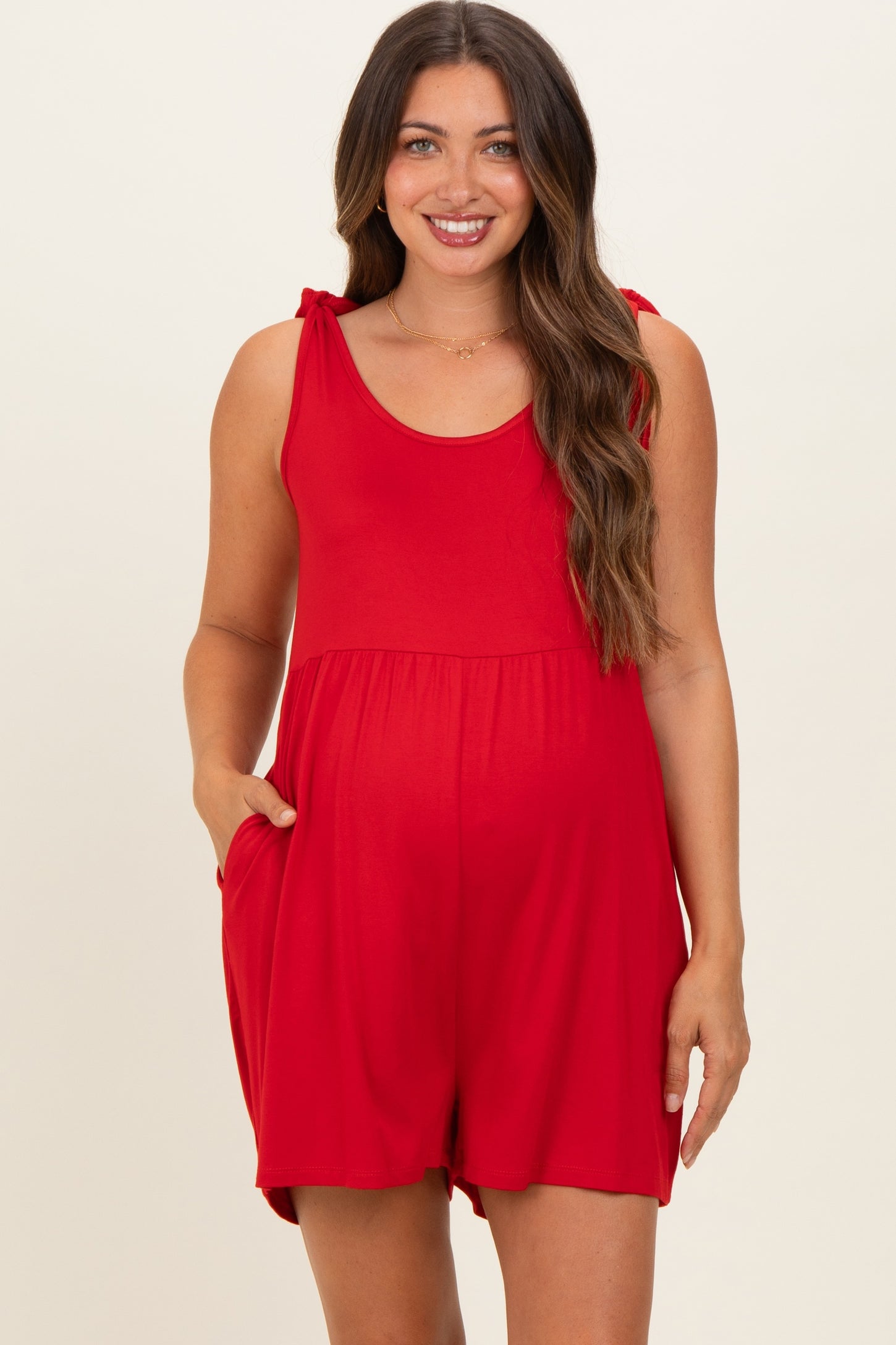 woman wearing a red maternity romper with tie straps and pockets, showcasing her baby bump