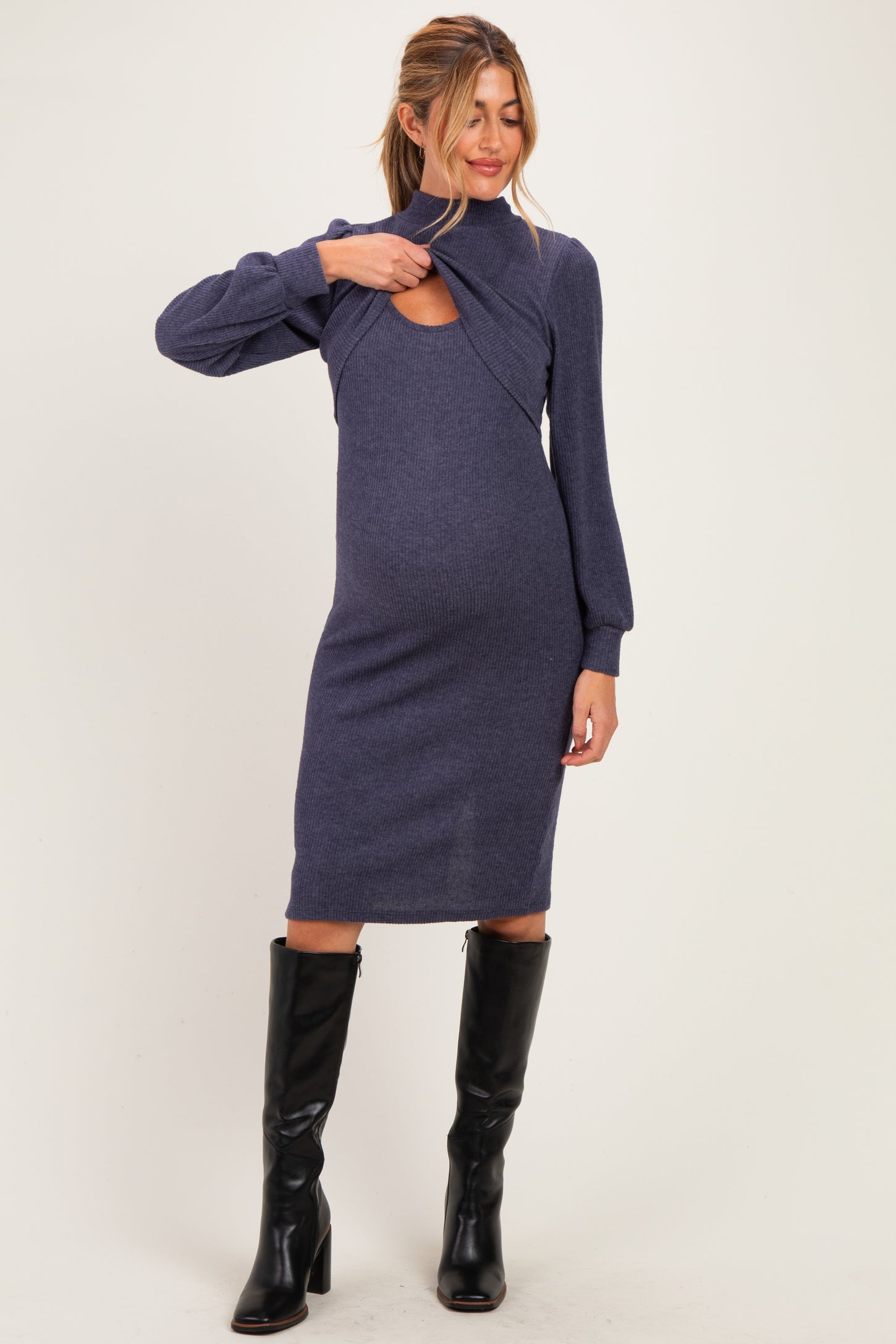 woman wearing a dark blue maternity dress with cut-out detailing and long sleeves, showcasing her baby bump