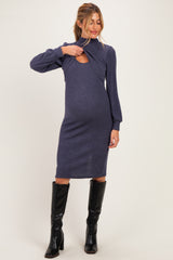 woman wearing a dark blue maternity dress with cut-out detailing and long sleeves, showcasing her baby bump