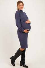 woman wearing a dark purple maternity dress with a fitted silhouette and holding her baby bump