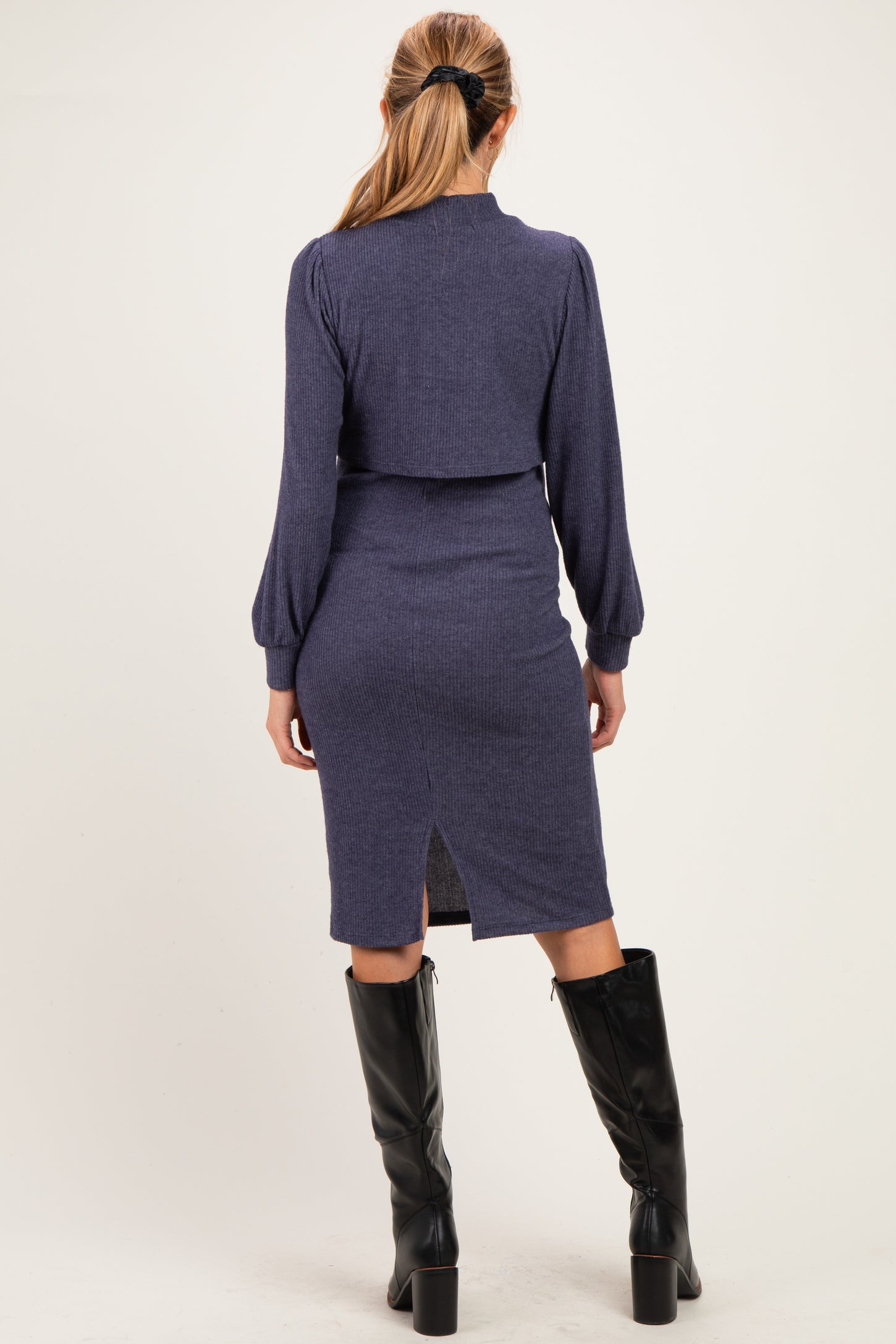 woman wearing a navy blue maternity dress with a fitted silhouette and long sleeves, featuring a back slit