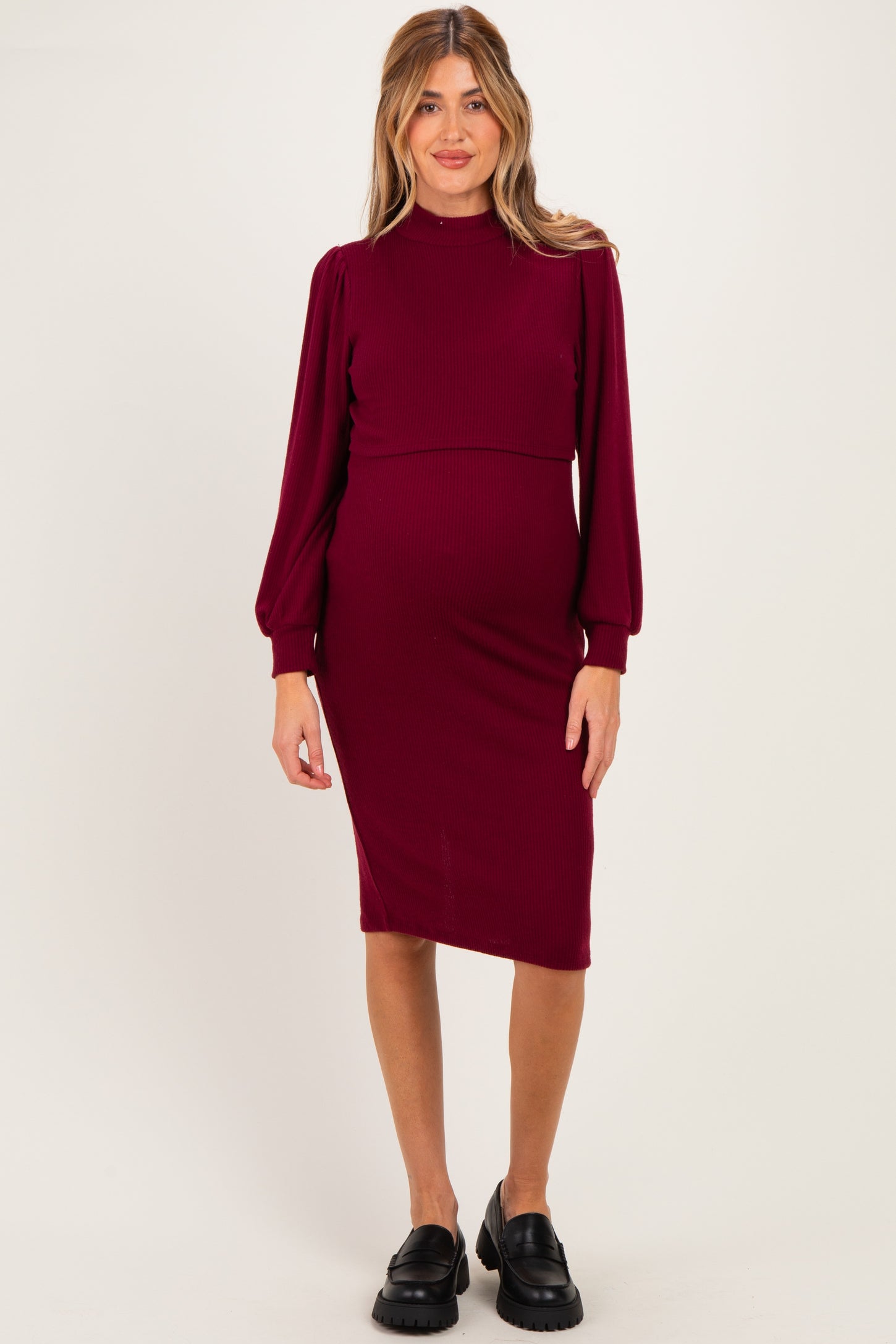 woman wearing a burgundy ribbed maternity dress with long puff sleeves and a fitted silhouette, showing her baby bump