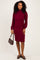 woman wearing a burgundy ribbed midi dress with long puff sleeves and a fitted skirt, holding a small brown handbag