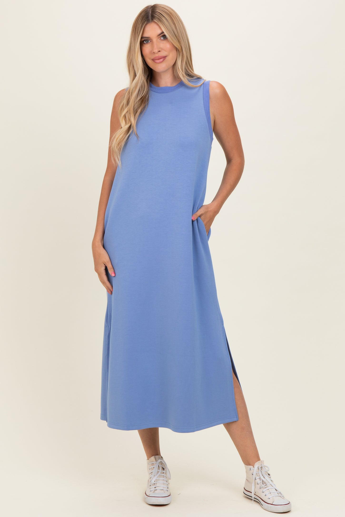 woman wearing a sleeveless light blue maxi dress with side pockets and side slits, styled with white sneakers