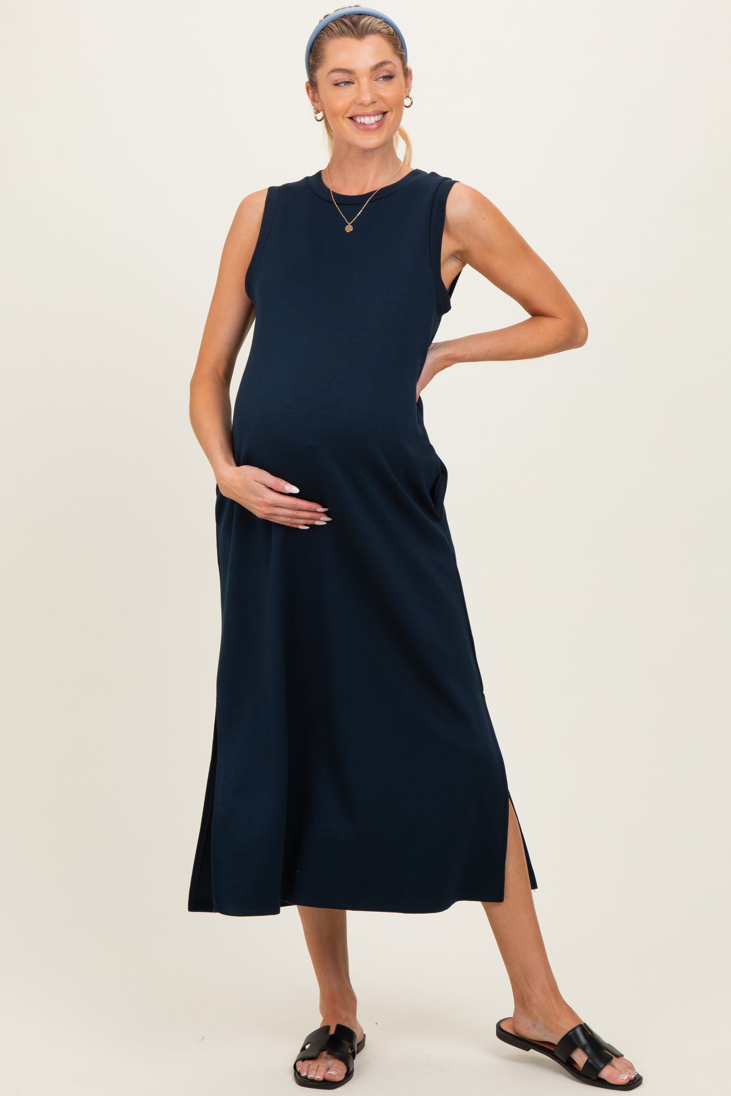 woman wearing a navy blue sleeveless maternity dress with side slits and holding her baby bump