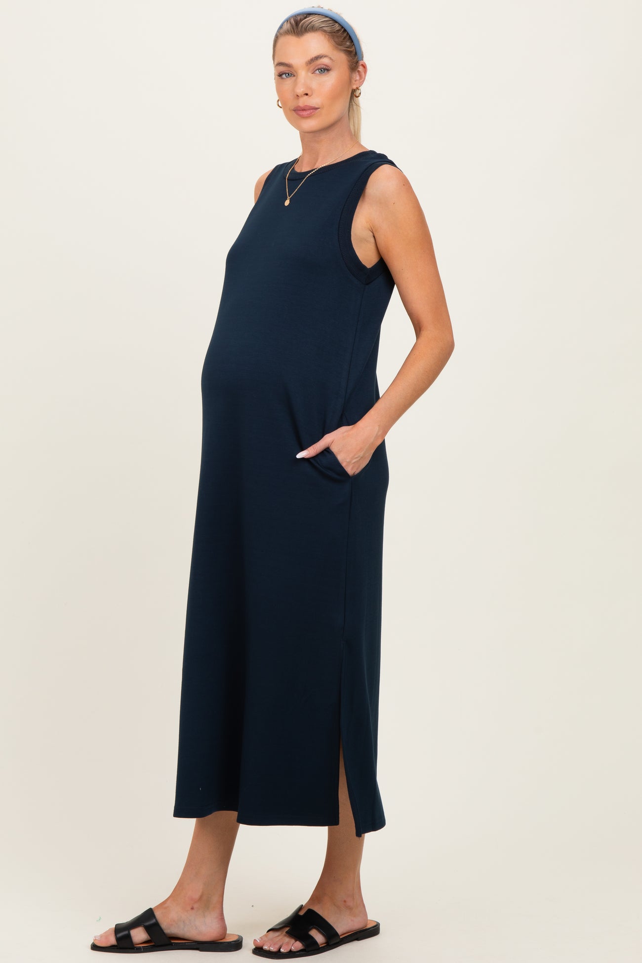 woman wearing a navy blue sleeveless maternity dress with side pockets and a side slit, showcasing her baby bump