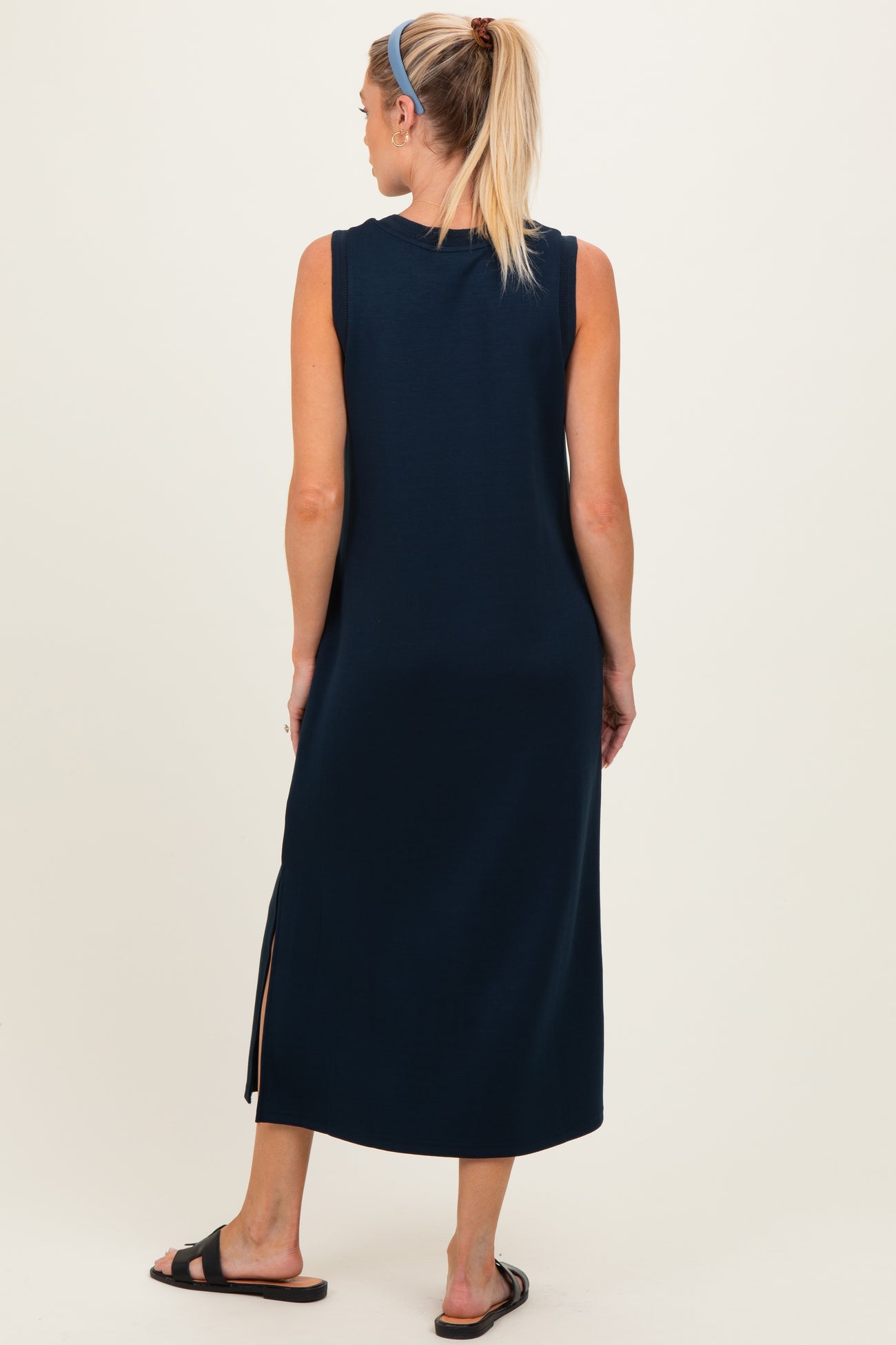 woman wearing a navy blue sleeveless maternity maxi dress with side slits, standing with her back to the camera