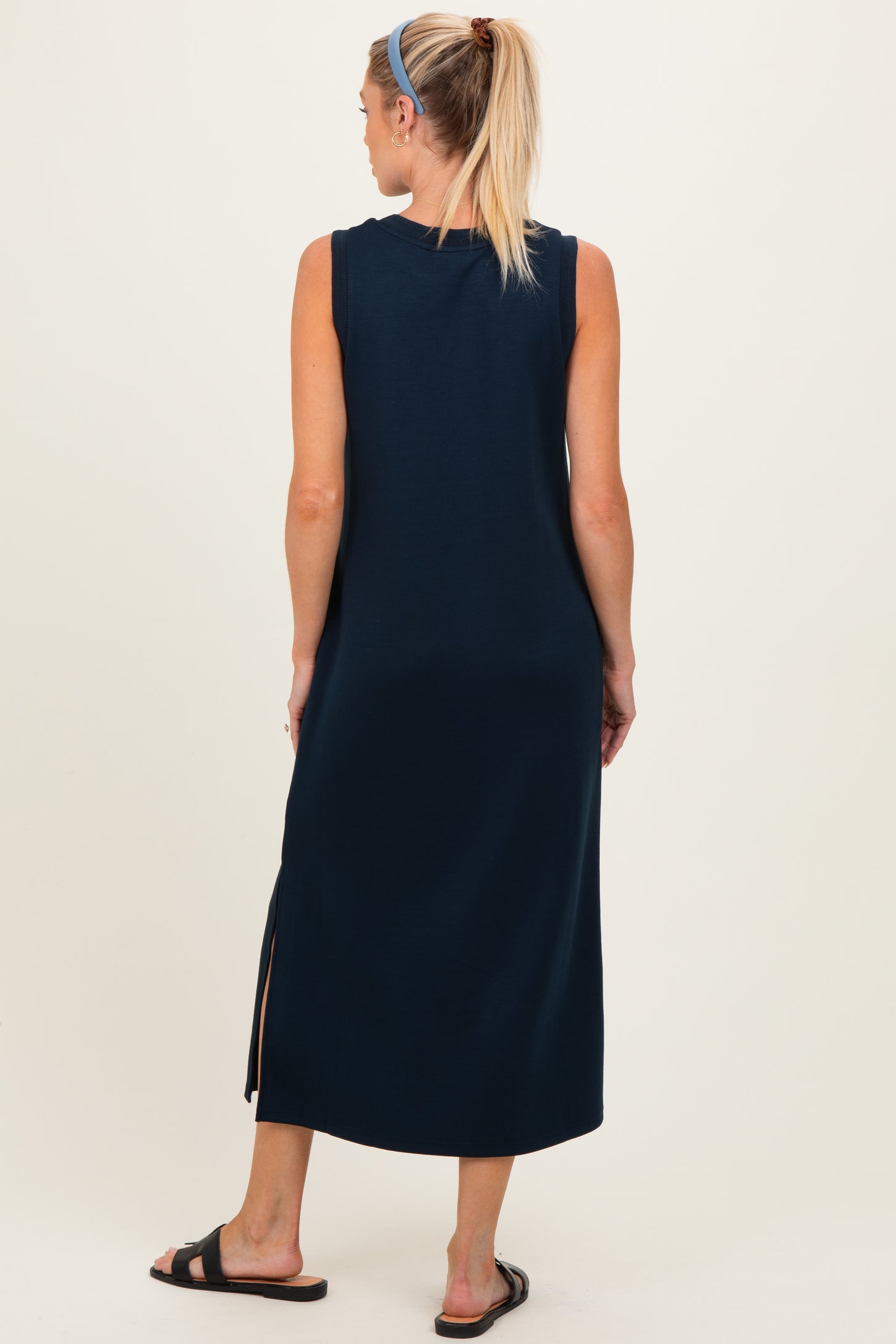 woman wearing a navy blue sleeveless maternity maxi dress with side slits, standing with her back to the camera