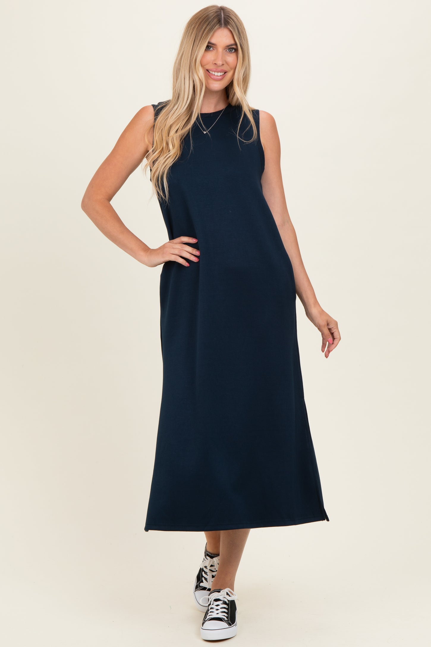 woman wearing a navy blue sleeveless maxi dress paired with black and white sneakers
