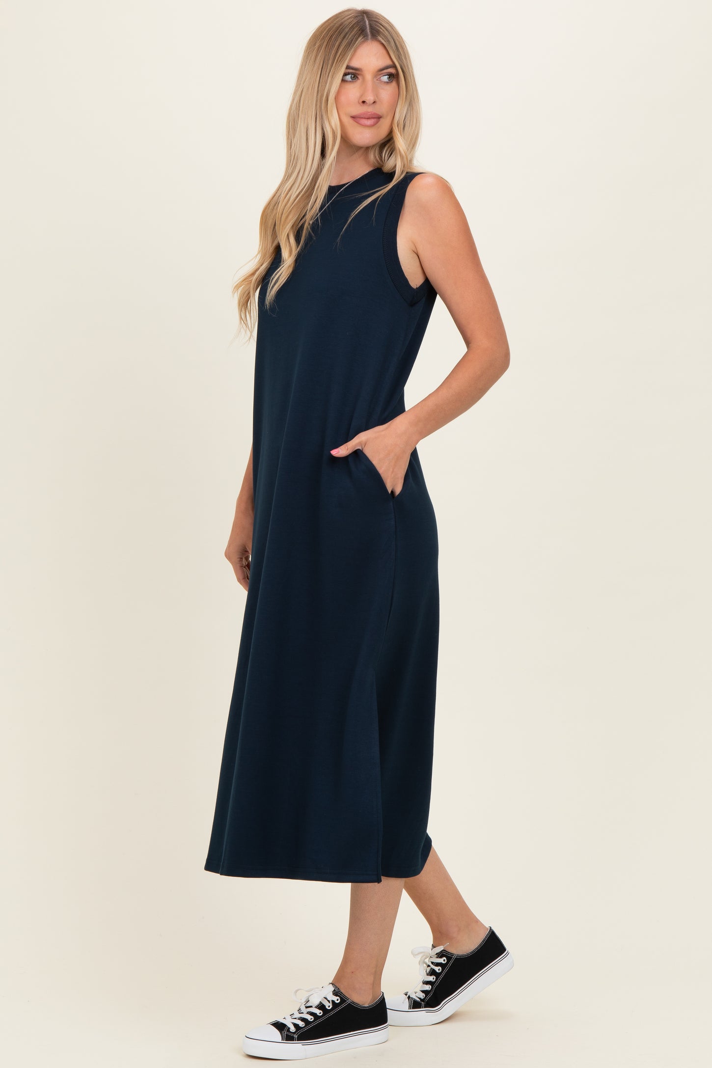 woman wearing a navy blue sleeveless maxi dress with side pockets and black sneakers