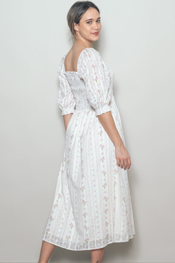 woman wearing a white floral midi dress with puff sleeves and a square neckline, standing sideways against a neutral background